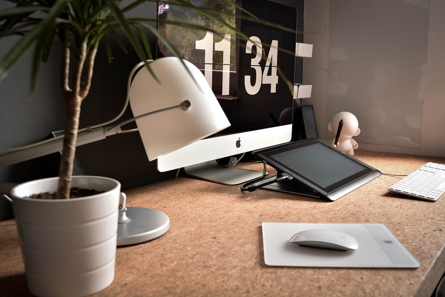 A creative workspace with a monitor, drawing tablet, lamp, and plants